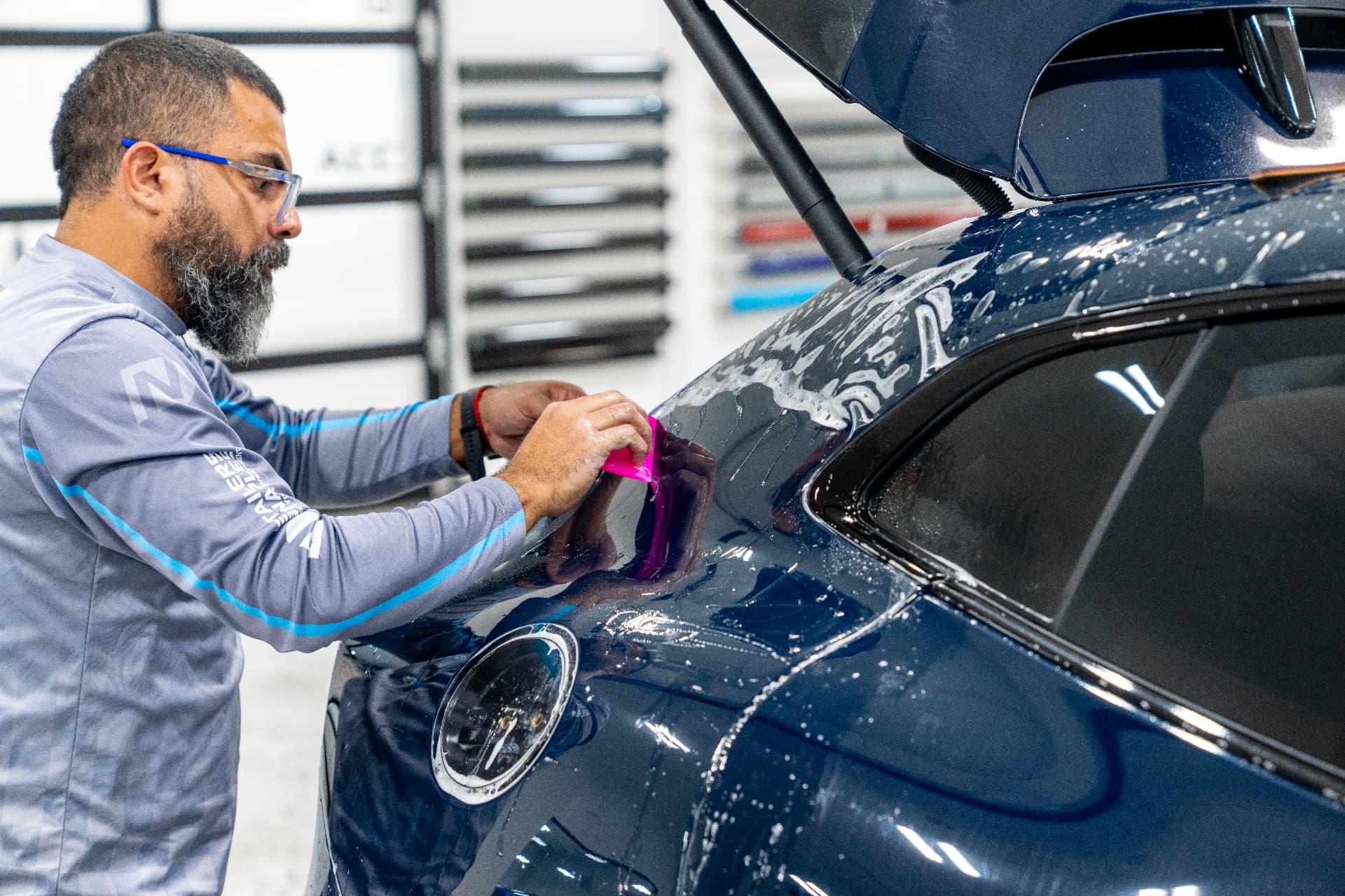Certified installer applying XPEL paint protection film to a dark blue vehicle in Naples