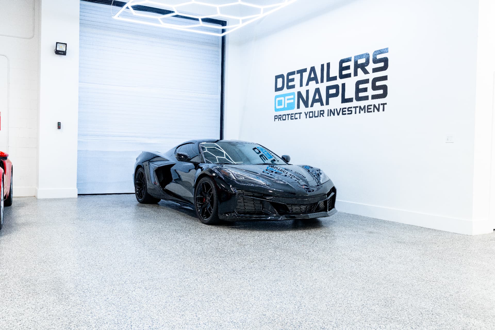 Black Corvette inside the Detailers of Naples facility with branded wall